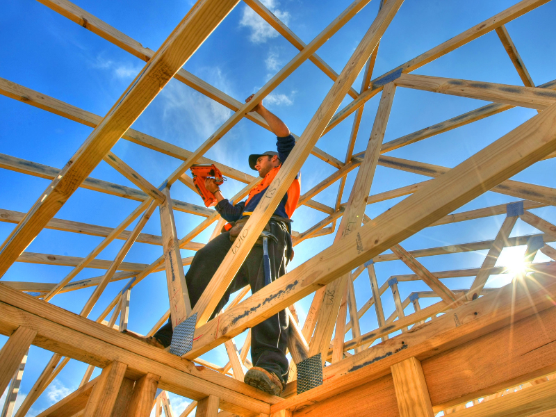 Construction worker nailing together a wooden house frame