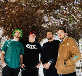 Four members of Buzzkill standing beneath a woven tunnel of branches and vines outdoors, wearing casual streetwear and looking toward the camera.
