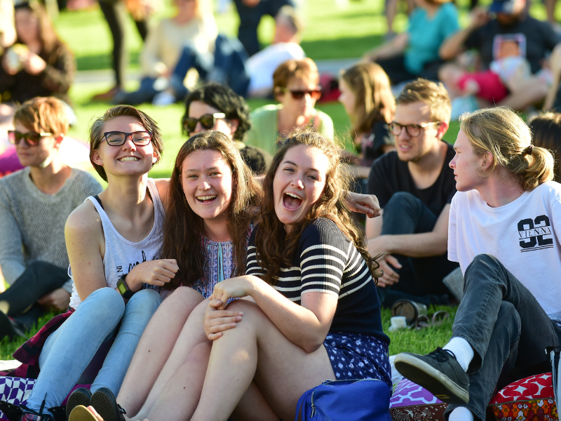 Three Young People huddled together sitting on a lawn in a crowd